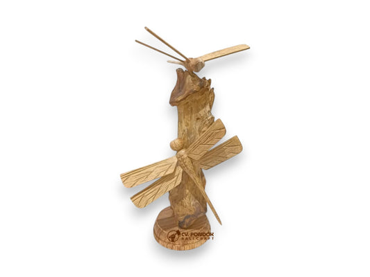 Two hand-carved wooden dragonflies with detailed wings displayed on a natural wooden trunk